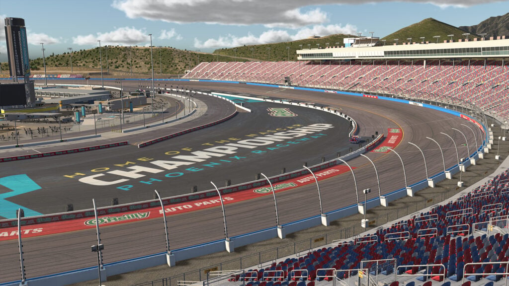A view of a race track at Phoenix Raceway with grandstands, empty seats, and "Championship" painted on the track. The area is surrounded by desert hills and a partly cloudy sky.